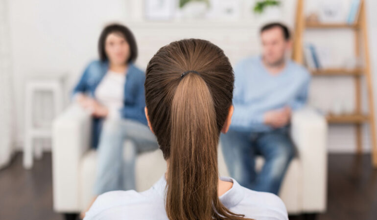 Couple and family psychology. Professional nice female psychologist sitting opposite her patients and looking at them while having a psychological session