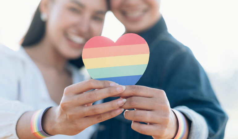 Close up hand of LGBTQ couple holding rainbow heart. LGBT rights concept.