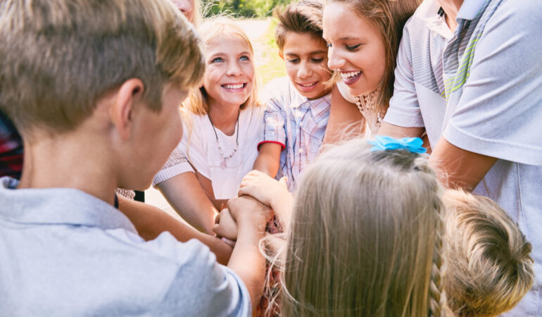 Happy children team heaping hands in summer. Friends or camp team before competition or game