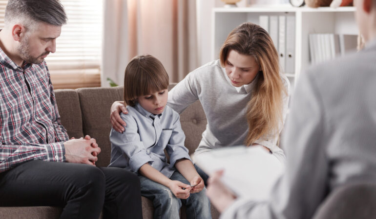 Mother hugging her autistic son, sitting next to a father during a family therapy